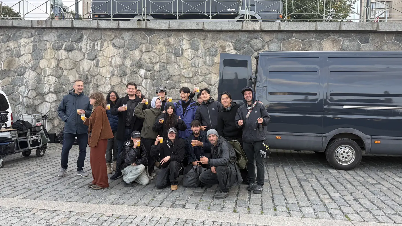 A mixed Asian and European film crew raising cups together in front of a production van at the end of a shoot day
