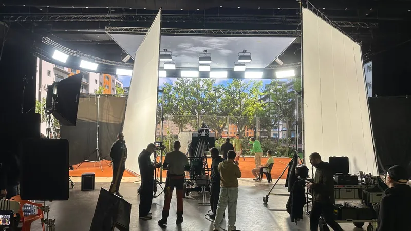 Film crew on a sound stage lighting a standing outdoor set through large diffusion frames